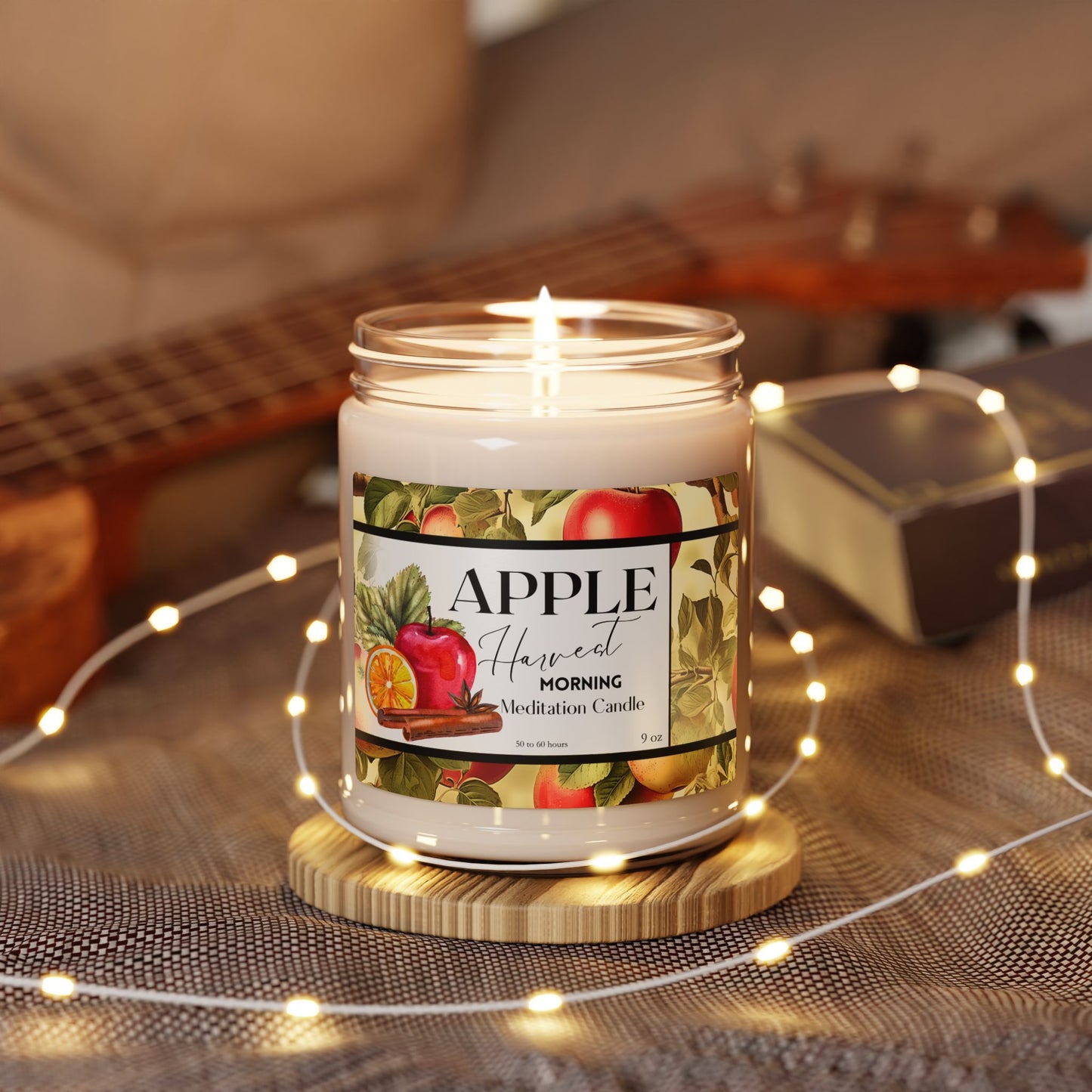 Lit candle in a jar with an 'Apple Harvest' label on a wooden coaster, surrounded by string lights.