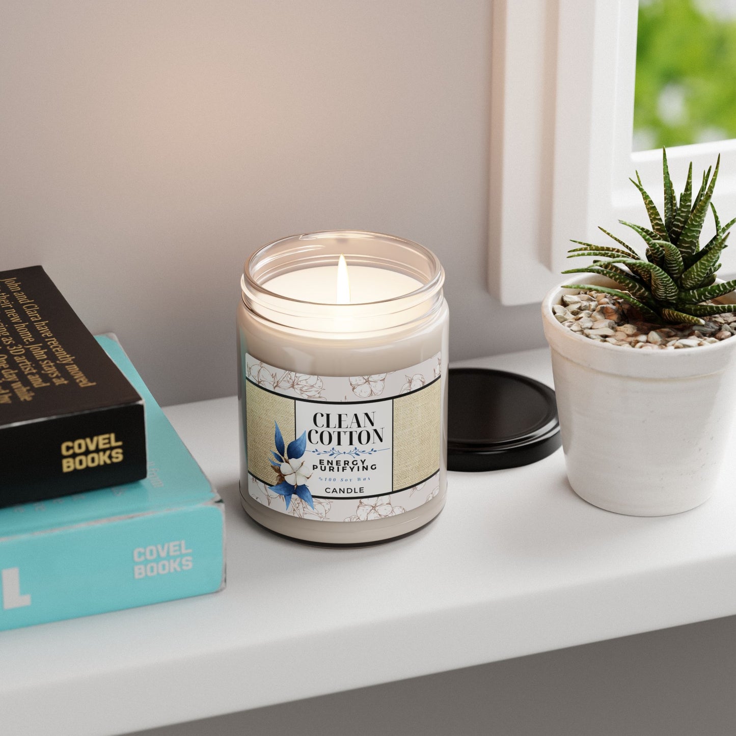Candle labeled 'Clean Cotton' on a shelf with books and a plant