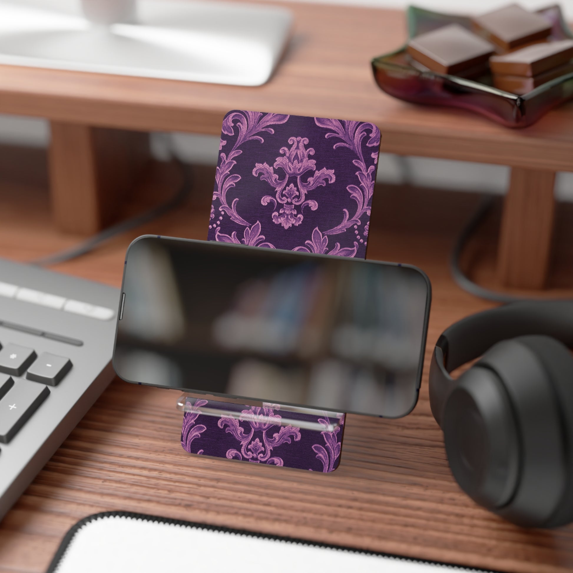 Phone stand with purple floral design on a desk with keyboard, mouse, and headphones.