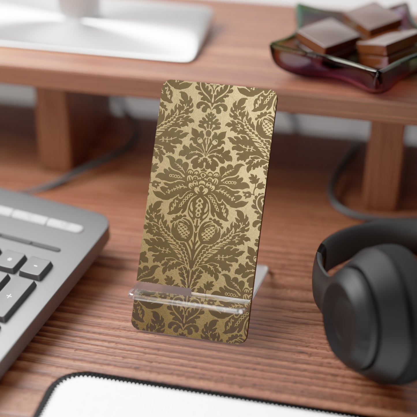 Decorative phone stand with gold pattern on a desk with keyboard, mouse, and headphones.