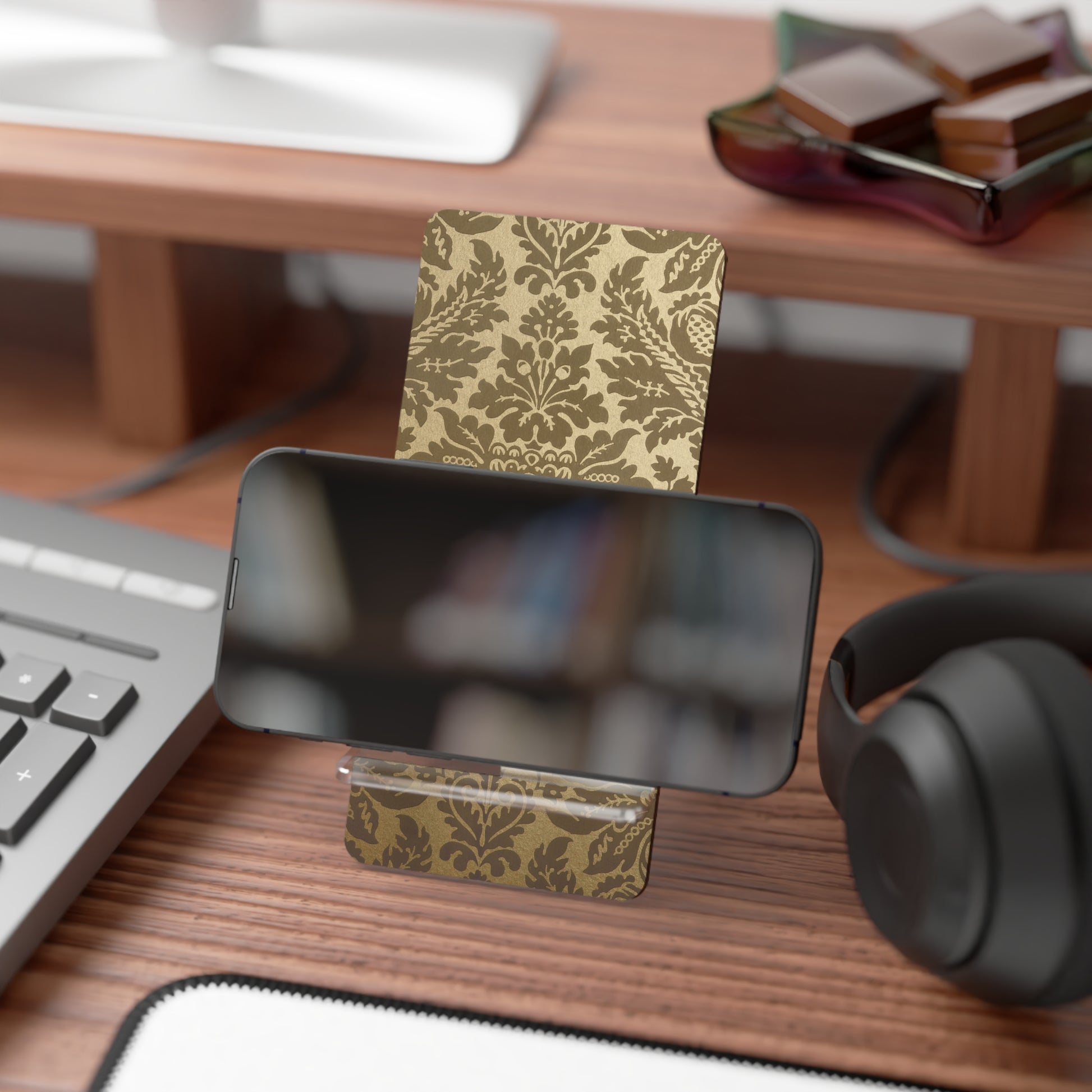 Decorative business card holder with gold pattern on a desk with keyboard, headphones, and books.