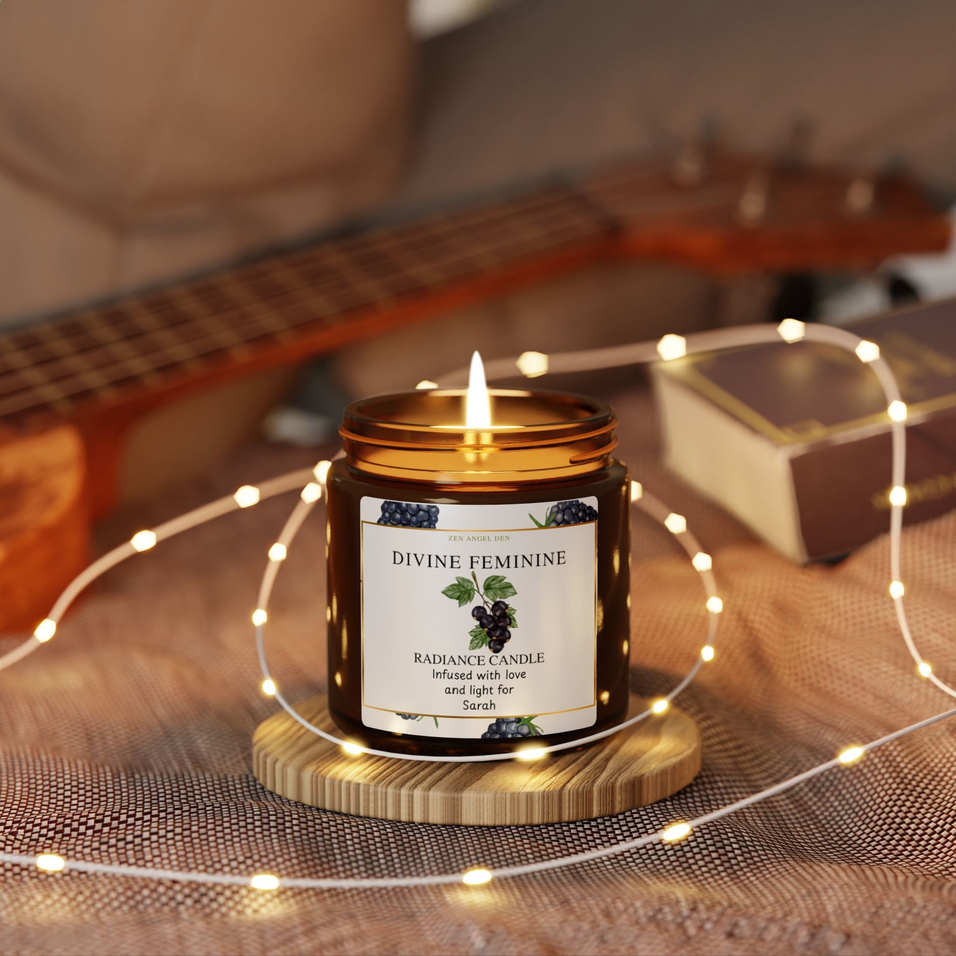 Candle labeled 'Divine Feminine' on a wooden stand with string lights and a guitar in the background.