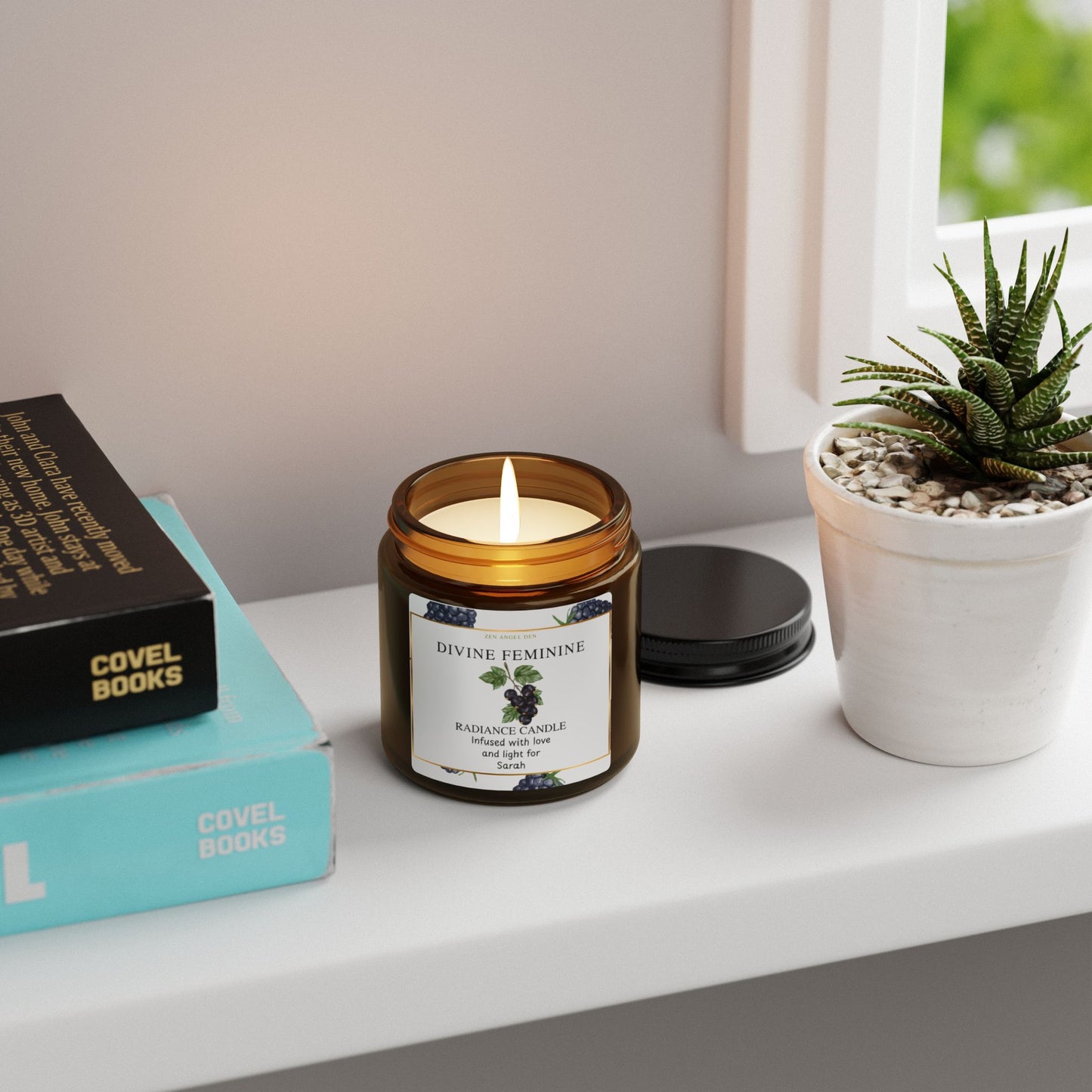 Candle labeled 'Divine Feminine' on a shelf with books and a plant