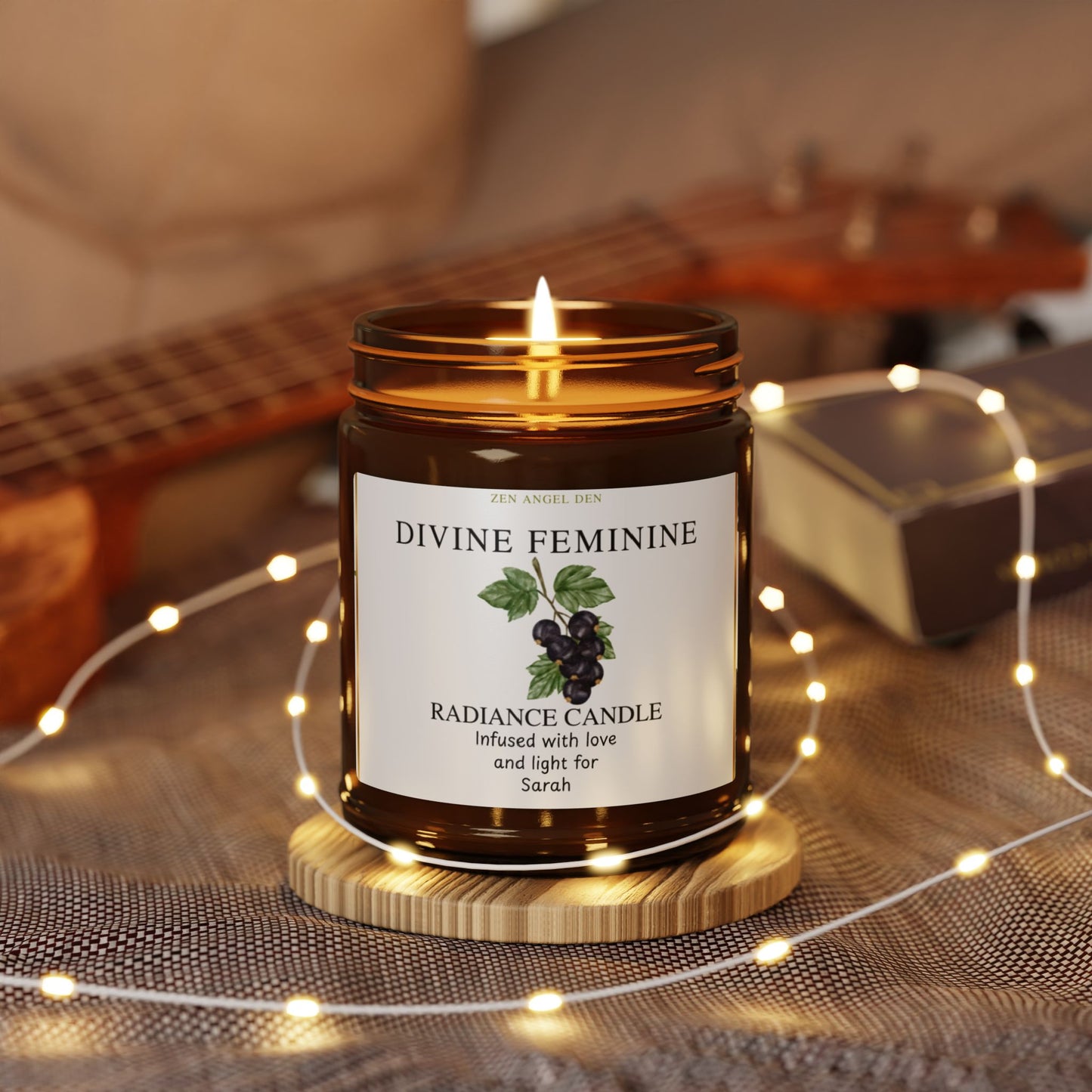 Divine Feminine candle on a wooden coaster with string lights and a guitar in the background