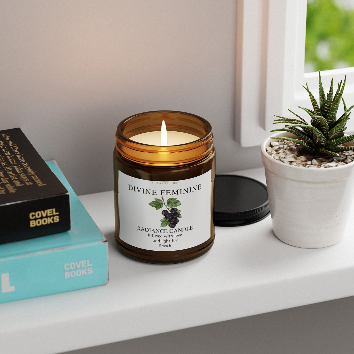 Candle labeled 'Divine Feminine' on a shelf with books and a plant