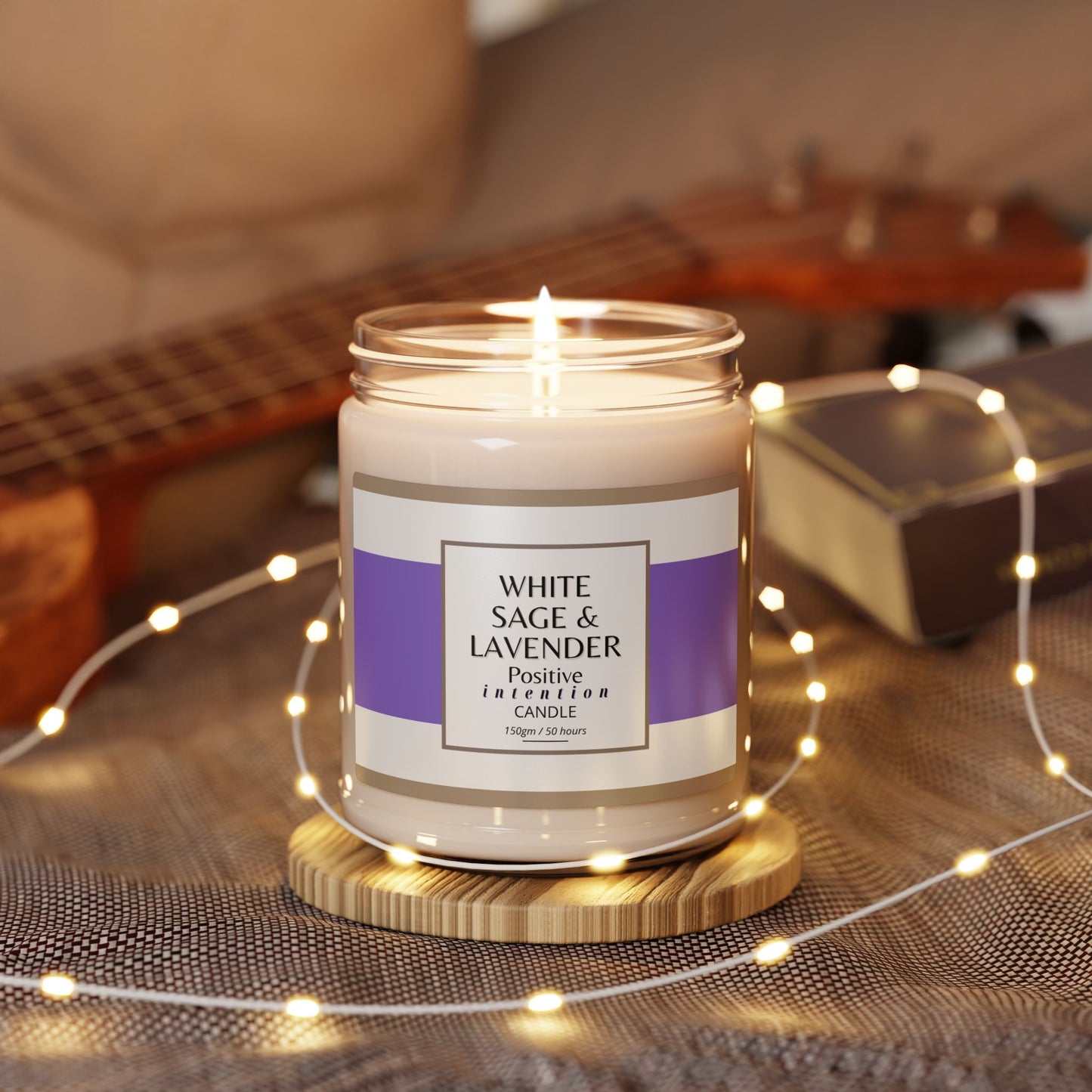 White sage and lavender candle with a label on a wooden coaster surrounded by string lights and a guitar in the background.